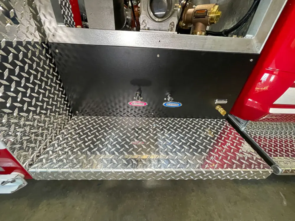 Exterior view of small fire truck showing cab, body compartments, and wheel/tire area.